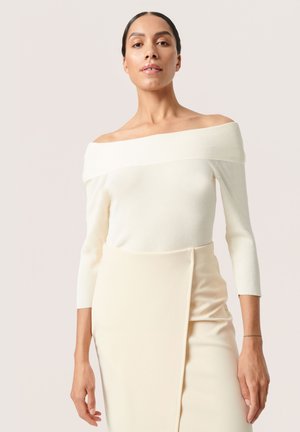 Schulterfreies, geripptes Strickoberteil in Creme mit Dreiviertelärmeln und einer glatten Textur, kombiniert mit einem hellen Cremetönigen Rock.