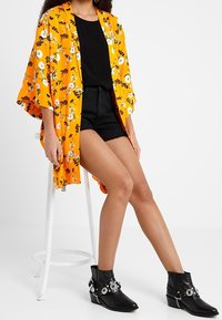 Orange floral kimono with loose sleeves, paired with a black top and shorts. Black ankle boots feature silver hardware accents.