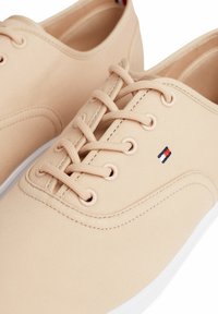 Beige kangaskengät pyöreällä varvalla, nauhakiinnityksellä ja valkoisella kumipohjalla. Ominaisuuksina hienovaraiset ompeleet ja pieni logo sivussa.