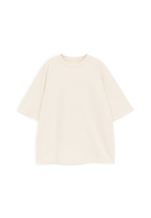 Sweatshirt ample à manches courtes de couleur blanc cassé, avec encolure ronde et manches raglan, posé à plat sur un fond blanc.