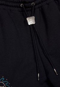 Zwarte katoenen sweatpants hebben een trekkoord met een metalen, vierkante hardwareaccent. De textuur is glad, met subtiele geborduurde details aan de zoom.