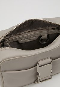 Szara skórzana torebka z zamkiem błyskawicznym, wewnętrzną kieszenią i metką z logo. Posiada metalowy detal z przodu.