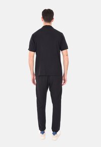T-shirt nera e pantaloni abbinati in tessuto morbido, caratterizzati da una vestibilità comoda. Sneakers bianche con dettagli blu completano l'outfit.