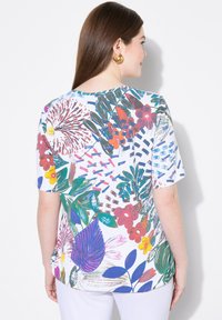 Top de manga corta con un patrón floral en rojo, azul, verde y amarillo sobre un fondo blanco; textura suave y corte relajado.