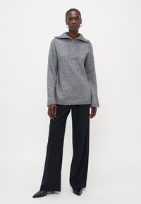Maglione grigio a maglia con colletto alto e zip, caratterizzato da un design a yoke testurizzato. Abbinato a pantaloni neri a gamba larga e scarpe a punta.