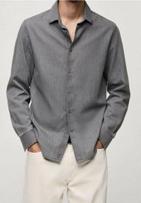 Grauhemd aus strukturiertem Stoff mit langen Ärmeln, Kragen und gerader Saum. Trägt man mit hellen Hosen.