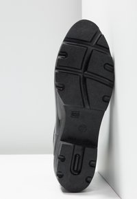 Semelle de chaussure noire à crampons profonds, taille 37 indiquée, avec l'inscription "Made in China" embossée sur une surface lisse, sur fond blanc et gris.