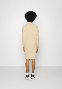 Abito lavorato a maglia beige con maniche lunghe, scollatura a costine e silhouette aderente, abbinato a sneakers bianco e nero e calzini alla caviglia bianchi.