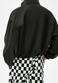 Svart satäng bomberjacka med hög krage och elastisk nederkant, matchad med byxor i kontrasterande svart och vitt rutmönster.