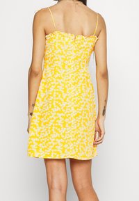 Keltainen kukkamekko, jossa on spagettiolkaimet, röyhelökaulus ja kukkakuosi. Valmistettu kevyestä kankaasta, mekko istuu vartalonmyöteiseksi.