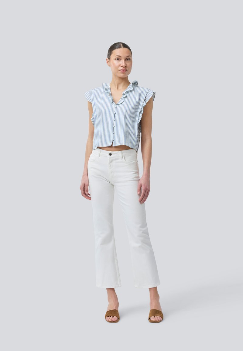 Camicia a maniche corte a righe blu chiaro e bianco, con maniche a volant, abbinata a jeans bianchi a campana e sandali aperti marroni.