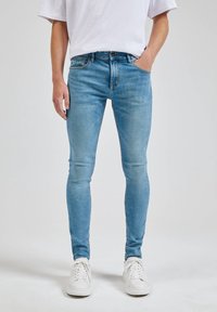 Úzké džíny ve světle modrém denimu, s klasickým pětipocket designem a jemným vyblednutím, spárované s bílými teniskami.