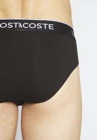 Schwarze Baumwollunterhose mit weicher Textur und elastischem Bund, der ein kontrastierendes Logo aufweist. Glattes, minimalistisches Design ohne Muster.