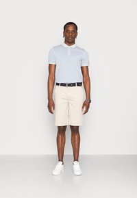 Lyseblå polo-skjorte med korte ærmer, hvid krave og logo, parret med beige shorts og hvide sneakers. Klassisk pasform, afslappet design.