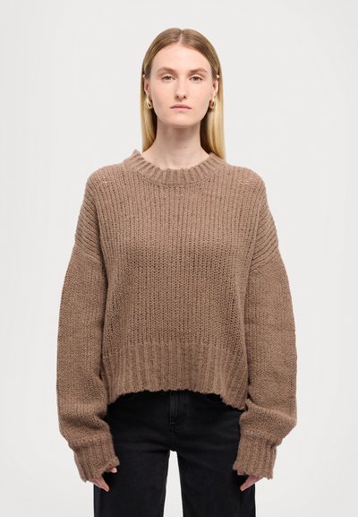 Suéter marrón de punto con cuello redondo y mangas largas y anchas. Presenta una textura acanalada y un dobladillo recortado. Se lleva con jeans negros.