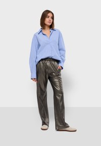 Lichtblauw gestreept overhemd met een oversized pasvorm; metallic grijze wijde broek; lichtgekleurde sneakers.