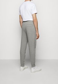 Pantalones de chándal grises con un ajuste ceñido, cinturilla elástica y puños. La tela parece suave con una textura lisa. Detalle del bolsillo trasero visible.