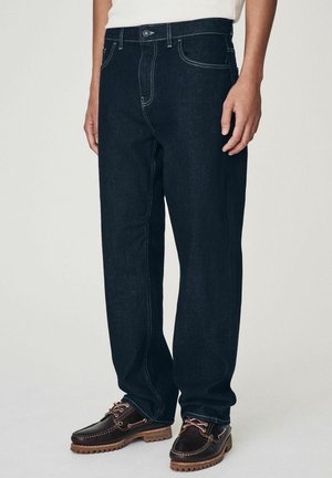 Mörkbla denimjeans med rak bendesign, synlig sömnad, framfickor och knäppning, tillsammans med bruna läderskor.