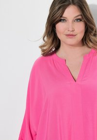 Tunic rosa con scollo a V e maniche corte. Realizzata in tessuto morbido, presenta una vestibilità comoda e sottili cuciture verticali per un tocco di stile.