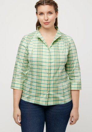 Camicia a quadri verde e gialla con colletto, maniche a tre quarti, chiusura con bottoni e texture liscia. Indossata con jeans blu scuro.