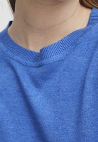 Gros plan sur le cou et les épaules portant un pull en maille bleu avec un col rond côtelé et échancré.