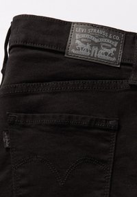 Vaqueros de mezclilla negros con un acabado texturizado, que cuentan con un parche trasero de cuero gris con detalles del logo, costuras en contraste y un diseño clásico de bolsillos.