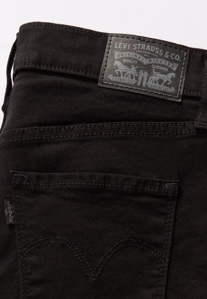 Jean en denim noir avec une finition texturée, ornés d'une patch en cuir gris au dos avec des détails de logo, des coutures contrastées et un design de poche classique.