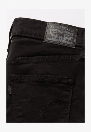 Jean en denim noir avec une finition texturée, ornés d'une patch en cuir gris au dos avec des détails de logo, des coutures contrastées et un design de poche classique.