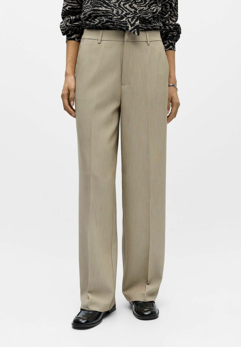 Szerokie spodnie w jasnym beżu z subtelnymi paskami, z paskami do paska i dopasowaną konstrukcją, w połączeniu z czarnymi pantoflami.