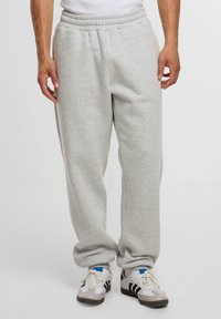 Helle graue Jogginghose mit einem elastischen Bund, lockerer Passform und seitlichen Taschen, kombiniert mit weißen Sneakers mit schwarzen und blauen Akzenten.