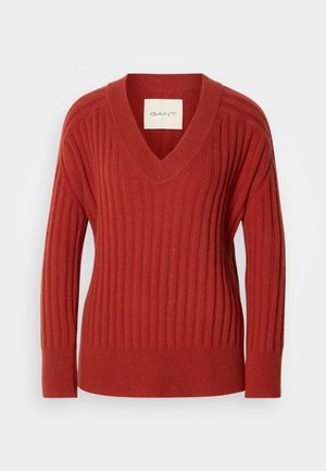 Sarkanais ribotais džemperis ar V veida kakla izgriezumu, garām piedurknēm un pieguļošu jostasvietu. Izgatavots no mīksta, strukturēta materiāla. Birka redzama iekšpusē ap kakla izgriezumu.