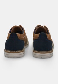 Pantofi din piele maro și suede bleumarin cu un profil jos, având talpă bej și un detaliu decorativ de cusătură pe toc.