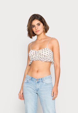 Top cropped de poás em bege claro com pontos em azul-marinho; apresenta franzidos, uma bainha com folhos e alças finas ajustáveis, combinado com jeans azul claro.
