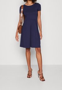Abito blu navy a maniche corte con corpino aderente e gonna svasata. Tessuto morbido, caratterizzato da un collo rotondo e delicate pieghe.