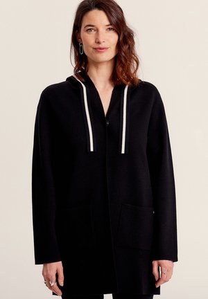 Manteau long noir avec une capuche et deux poches avant. Comprend des cordons réglables rayés blancs, une patte de boutonnage et une coupe décontractée. Texture douce.