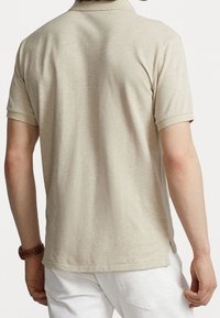 Beżowa koszulka polo z krótkimi rękawami, o teksturowanej tkaninie i klasycznym kołnierzyku. Posiada boczne rozcięcia i prosty krój na dole.