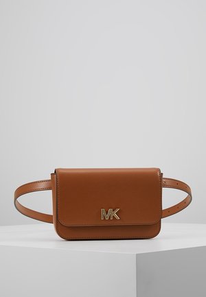 Sac ceinture en cuir marron avec logo MK doré sur le rabat avant, présenté sur un socle blanc avec un fond gris uni.