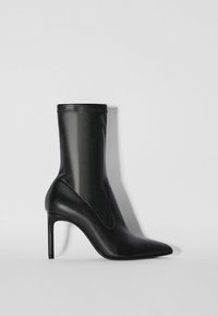 Svart läderankelboots med spetsig tå, smal hög klack, slät yta och elastiskt övre kant, med en elegant och minimalistisk design.