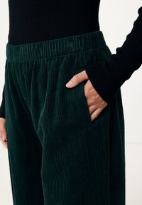 Gröna kordfløyelpant med ribbad textur, med elastisk midja och sidofickor. Kombinerat med en svart långärmad topp.