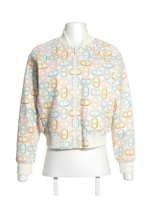 Veste bomber blanche avec des motifs multicolores en forme de pilule, poignets, col, ceinture côtelés et une fermeture éclair frontale sur un torse de mannequin blanc.