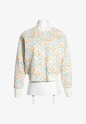 Veste bomber blanche avec des motifs multicolores en forme de pilule, poignets, col, ceinture côtelés et une fermeture éclair frontale sur un torse de mannequin blanc.