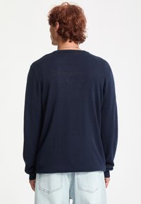 Mørkeblå langærmet sweater lavet af et struktureret strikket stof, med en rund halsudskæring og ribkant ved ærmer og nederkant.