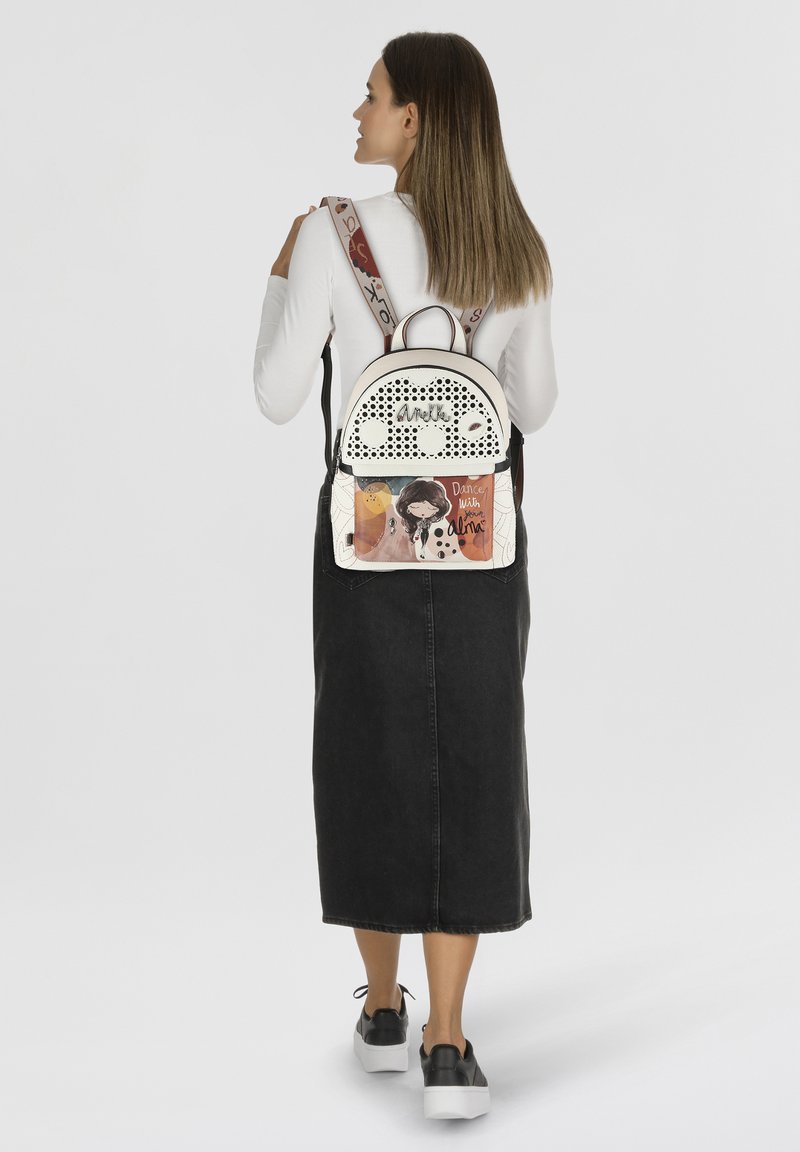 Sac à dos blanc et noir avec des accents perforés, design illustré représentant une fille, et bretelles réglables. Poignée supérieure amovible.