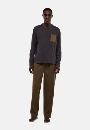 Chemise grise à manches longues avec une poche marron, associée à un pantalon large vert olive. Texture lisse, coupe décontractée et design minimal.