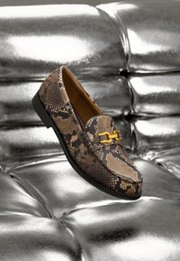 Mocassins à motif peau de serpent marron et noir avec un accent en métal doré, présentant une texture lisse et une semelle basse noire.