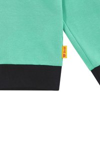 Felpa verde con finitura testurizzata, dotata di polsini neri e un'etichetta gialla del brand. Il materiale sembra morbido e leggero.