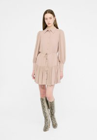 Abito a manica corta di un leggero beige, con un bottone frontale, vita legata e orlo a strati. Indossato con stivali a coscia in pelle di serpente.