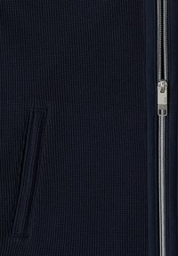 Nærbillede af tekstureret mørkeblå stof med en lodret sølvlynlås til højre og en lodret lomme til venstre.