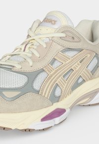 Μπεζ και γκρι αθλητικό παπούτσι ASICS με λευκό δίχτυ, κρεμ κορδόνια και μοβ λεπτομέρεια στη σόλα, από μπροστινή πλευρά.