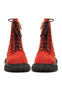 Paire de bottines montantes en daim rouge vif avec semelles épaisses en caoutchouc noir, vues de face sur un fond blanc.